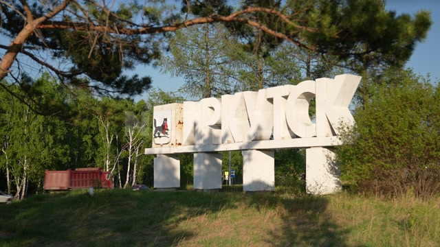 Стела "ИРКУТСК" на въезде в город, в кадре большие белые буквы, герб города, загородное шоссе