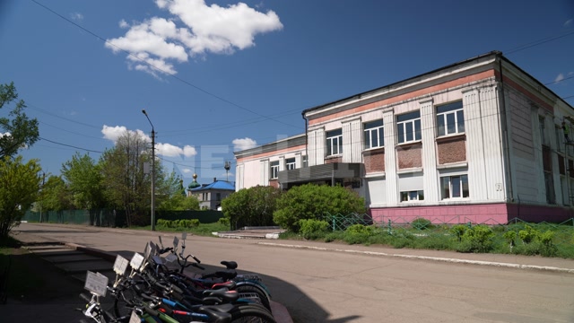 Провинциальный город, лето, день, в кадре двухэтажное здание, велосипедная парковка