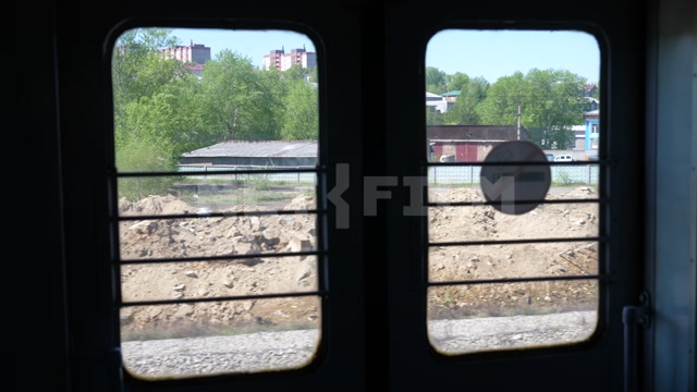 Вид из окна электрички, проезд под мостом, в кадре насыпь, одноэтажные постройки, промзона