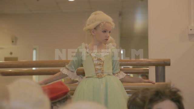 A rehearsal room at a ballet school, with a girl in a dress and wig near a barre