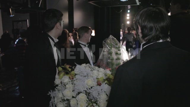 Мужчины в черных костюмах с бабочками стоят за кулисами с цветами