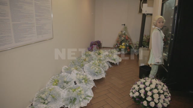 An office, with bouquets and baskets of flowers on the floor. In the room are ballet school