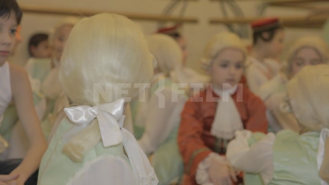 The frame shows children (students of the ballet school) in stage costumes and wigs before the