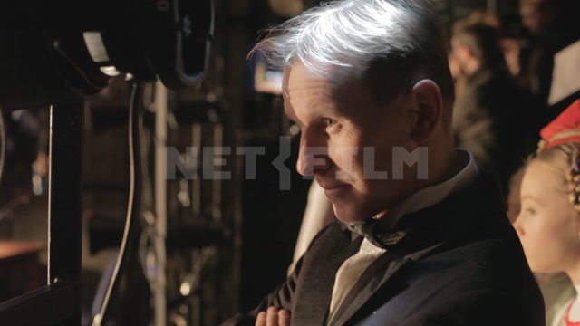 A man watches the stage from behind the curtains