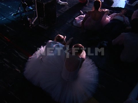 Young ballet dancers backstage, in stage costumes, sitting on the floor, stretching, and resting